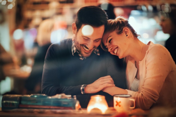 Eine Frau und ein Mann sitzen in einer Bar. Die Frau legt ihren Kopf auf die Schulter des Mannes.