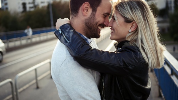 Eine Frau und ein Mann stehen auf einer Brücke und umarmen sich. 